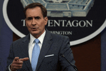 a man in a suit and tie stands in front of a sign that says pentagon