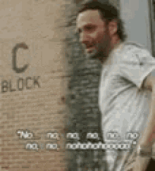 a man in a white shirt is standing in front of a brick wall with the word block on it .