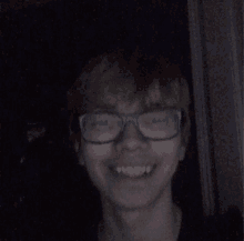 a young man wearing glasses is smiling in the dark