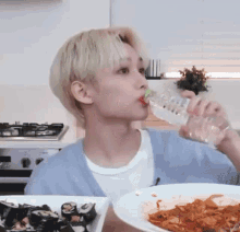 a young man is drinking water from a bottle while sitting at a table with a plate of food .