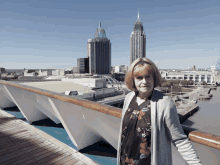 a woman stands on a deck with a city skyline behind her