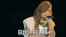 a woman singing into a microphone with the words " guys relax " on the bottom