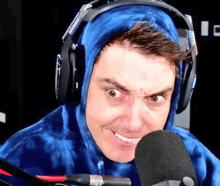 a man wearing headphones and a blue tie dye hoodie is smiling into a microphone .