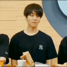 a young man wearing a black ny yankees t-shirt is sitting at a table with a bag of food .