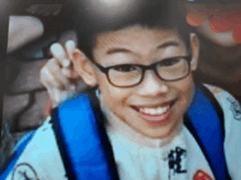 a young boy wearing glasses and a blue backpack smiles for the camera