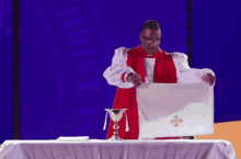 a priest in a red robe holds a white cloth with a cross on it