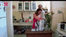 a woman in a pink tank top is standing in a kitchen next to a man in a white shirt