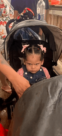 a little girl is sitting in a stroller with a bottle of water in the background