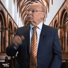 a man in a suit and tie stands in front of a church with the words heute show on the bottom right