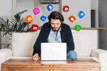 a man sits on a couch using a laptop with social media icons surrounding him