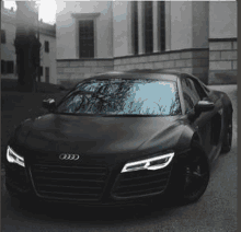 a black audi r8 coupe is parked in front of a building .