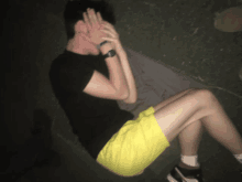 a man in a black shirt and yellow shorts is covering his face