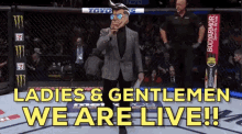 a man in a mask stands in a boxing ring with the words ladies & gentlemen we are live