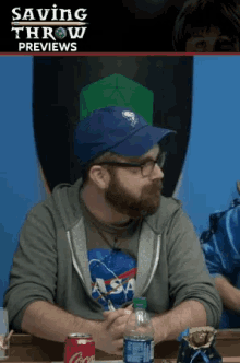 a man wearing a nasa shirt sits at a table with a bottle of water and a can of coca cola