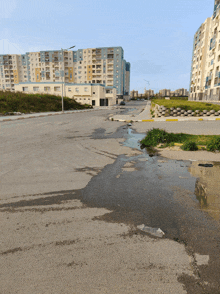 a puddle of water on the side of a road in front of tall buildings