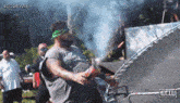 a man with a green bandana on his head is holding a lighter in front of a trampoline with the word gew on it