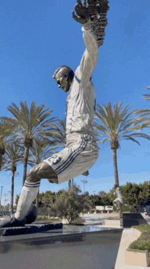 a statue of a man in a white shirt and blue shorts is jumping in the air with palm trees in the background