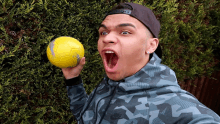 a man in a camouflage jacket is holding a yellow soccer ball