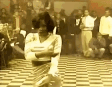 a woman is dancing on a checkered floor while a crowd watches .