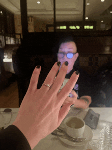 a woman 's hand with a ring on it and a man in the background with glasses