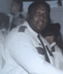 a man in a white uniform and tie is sitting in a car with other people .