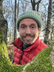 a man wearing a green hat and a red jacket is smiling in the woods