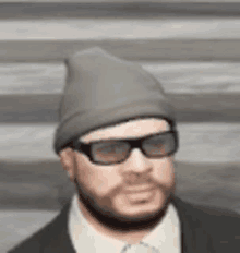 a man with a beard and sunglasses is wearing a beanie and a suit .