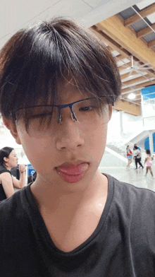 a young boy wearing glasses and a black shirt sticks his tongue out