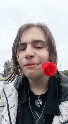 a man with a red rose in his mouth wearing a necklace with a pendant that has the letter l on it