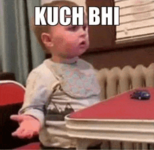 a baby is sitting at a table with his hands outstretched and a toy car on the table .