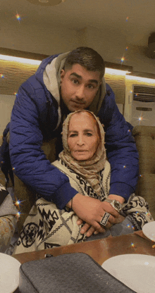 a man in a blue jacket hugs an older woman wearing a watch that says rolex