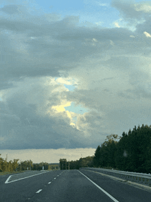 a highway with trees on both sides and a cloudy sky in the background