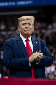 donald trump wearing a blue suit and red tie is clapping his hands