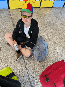 a man wearing sunglasses and a colorful hat sits on the floor holding a can of soda