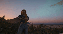 a screenshot of a video game shows a person standing in a field with a sunset in the background