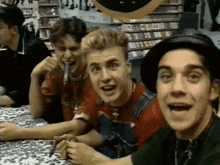 a group of young men are sitting at a table in a store and one of them is wearing overalls and a hat