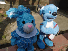 two blue stuffed animals are sitting on a brick wall