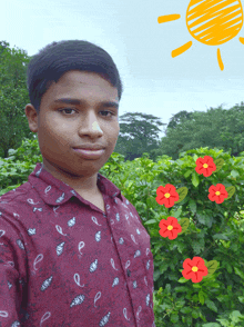 a young man stands in front of a bush with red flowers and a drawing of the sun