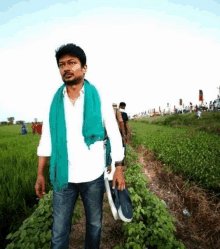 a man with a green scarf around his neck is standing in a field holding a pair of shoes