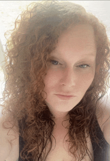 a woman with curly red hair and blue eyes looks at the camera