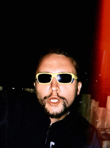 a man with a beard is wearing yellow sunglasses and a black jacket