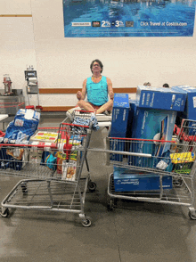 a man sits in a lotus position surrounded by shopping carts full of boxes including a samsung tv