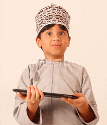 a young boy wearing a hat and holding a tablet with the word arabstock on the bottom