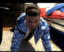 a boy wearing a blue camo jacket is doing pushups on the floor