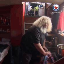 a man with blonde hair and a beard is washing dishes in a kitchen with omrop fryslan on the bottom right