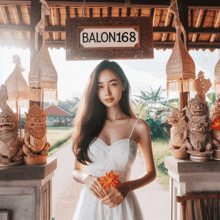 a woman in a white dress holds a flower in front of a sign that says balon168