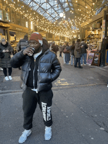 a man drinking a cup of coffee while wearing a black jacket and sweatpants that say lovers