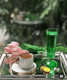 a cup of coffee sits on a tray next to a green glass