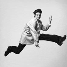 a black and white photo of a man in a coat jumping in the air