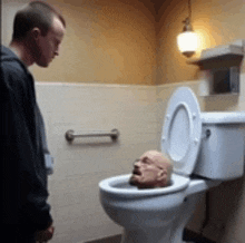 a man is standing next to a toilet with a head in it